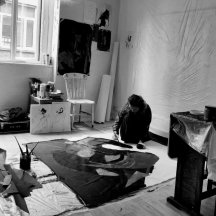 Black and white image of an artist in a studio with a canvas on the floor, painting